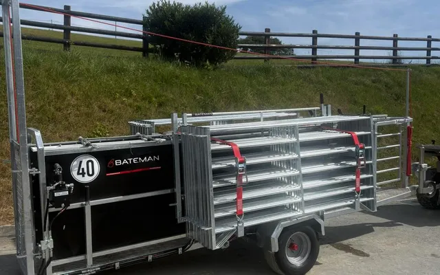 A Bateman sheep handling trailer loaded with galvanised hurdles and marked with the Bateman name, parked on a farm lane