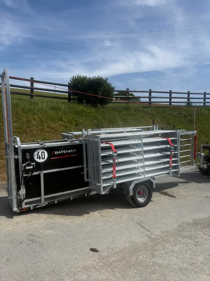 A Bateman sheep handling trailer loaded with galvanised hurdles and marked with the Bateman name, parked on a farm lane