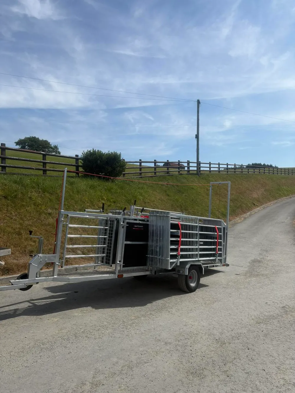 The loaded Bateman sheep handling trailer seen from behind on a farm lane, hurdles strapped along its length