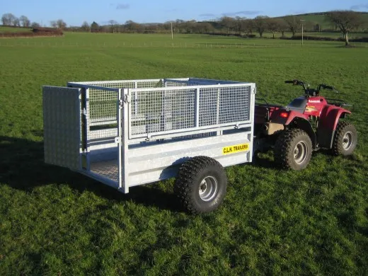 The mesh-sided ATV trailer hitched behind a quad in a field, tailgate closed