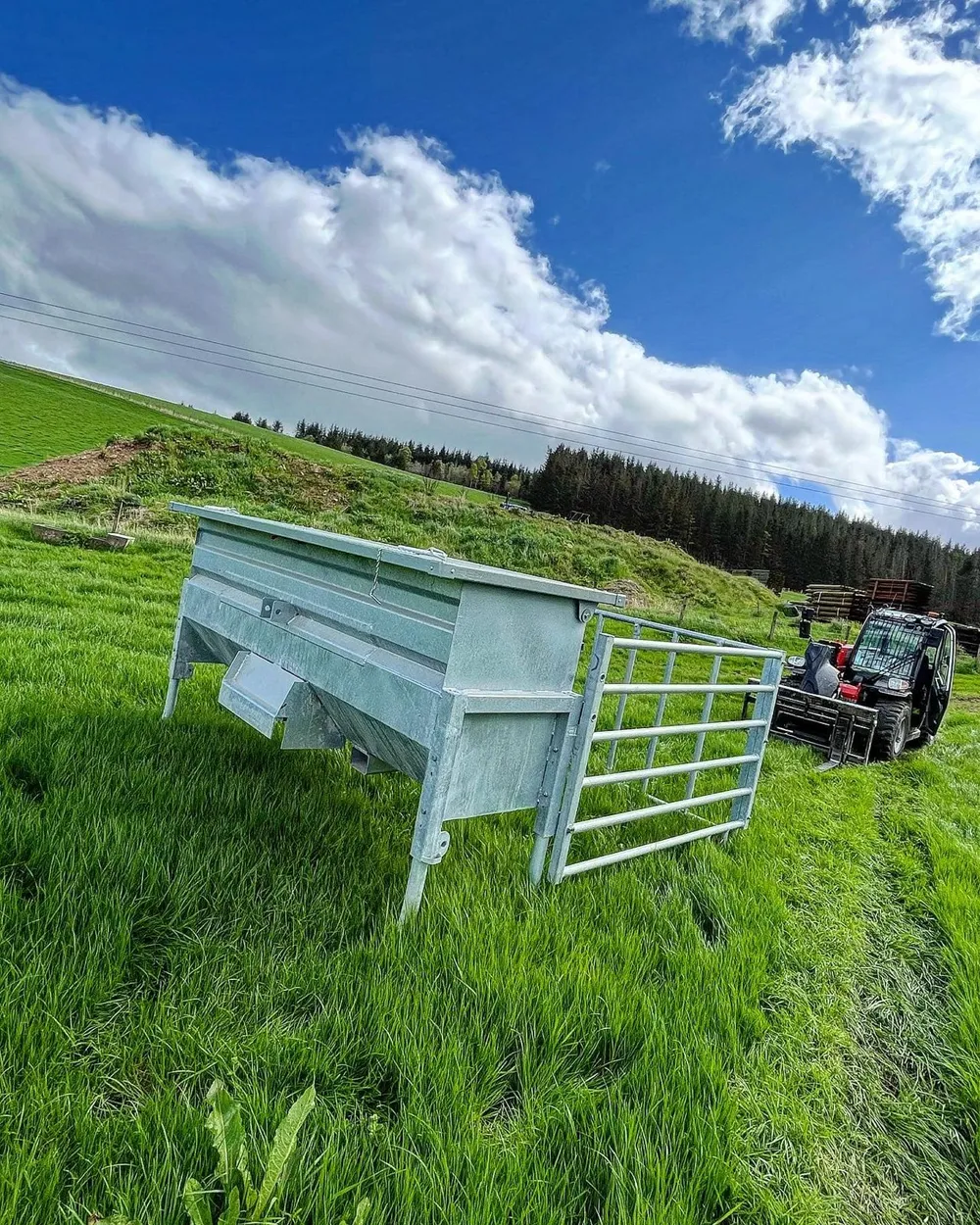 A galvanised creep feeder and its gate section set down in long grass, with the telehandler that placed them behind