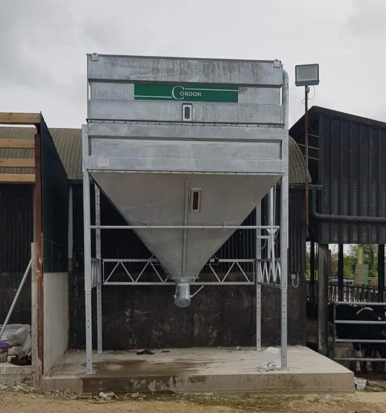 The bin head-on, raised on a concrete plinth beside a cattle shed