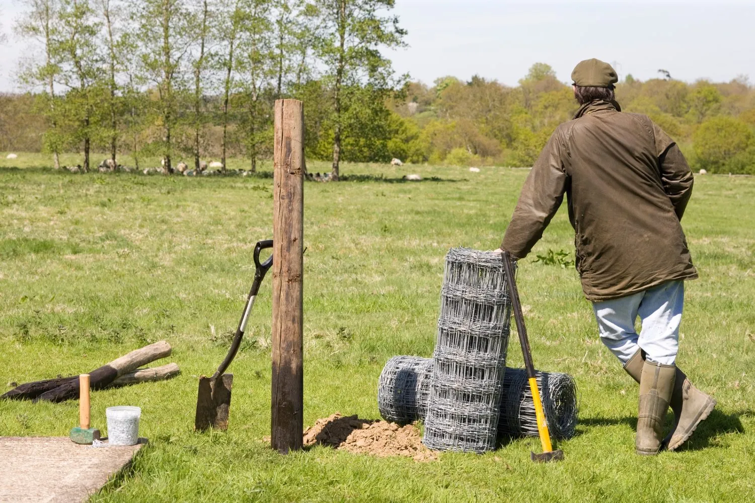 A farmer setting new stock fencing in a field, with a roll of wire and tools to hand