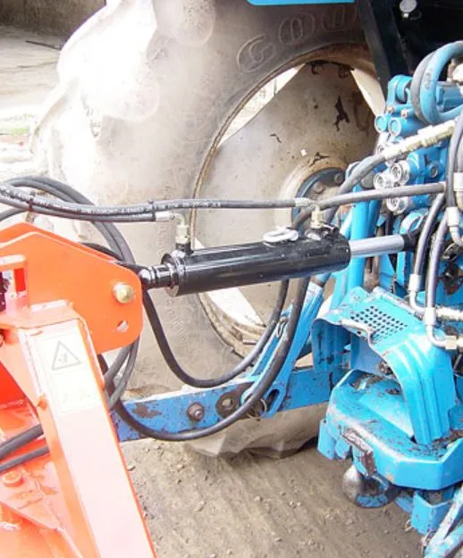 A hydraulic ram and hoses running between the knocker's frame and the tractor's rear linkage